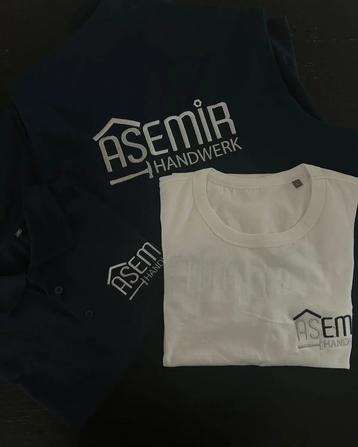 Bestickte Arbeitsjacke und weißes T-Shirt eines Handwerksbetriebs mit Logo auf Rücken und Brust