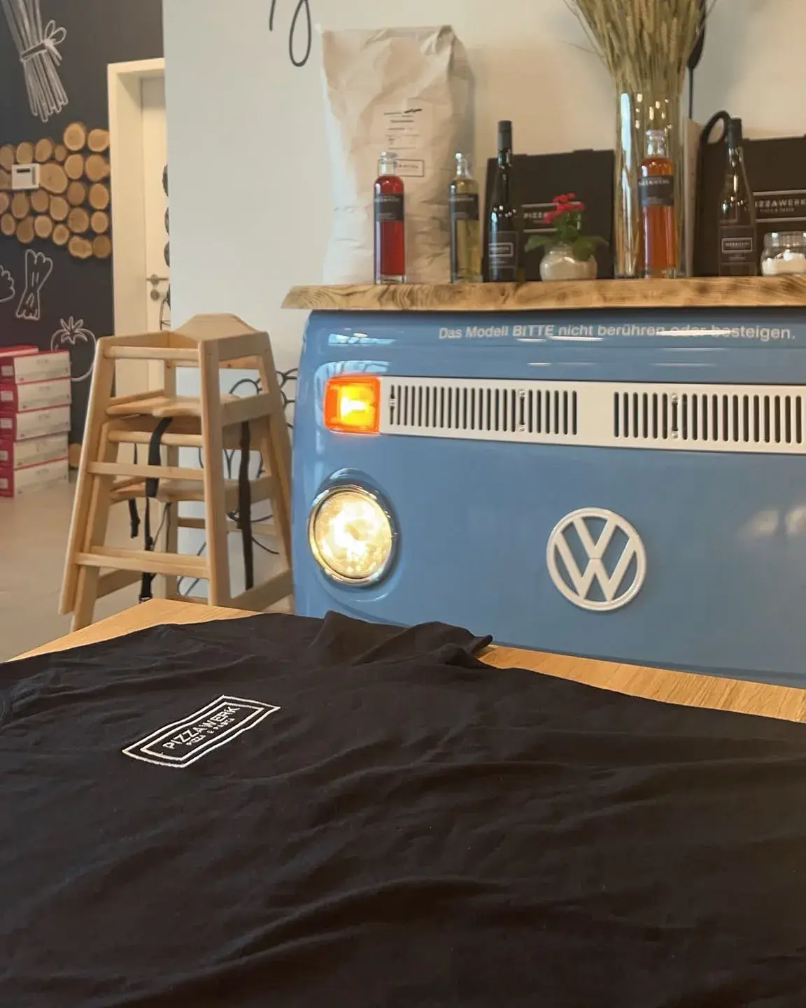 Schwarzes T-Shirt mit besticktem Brustlogo, abgelegt an der Theke beim Kunden