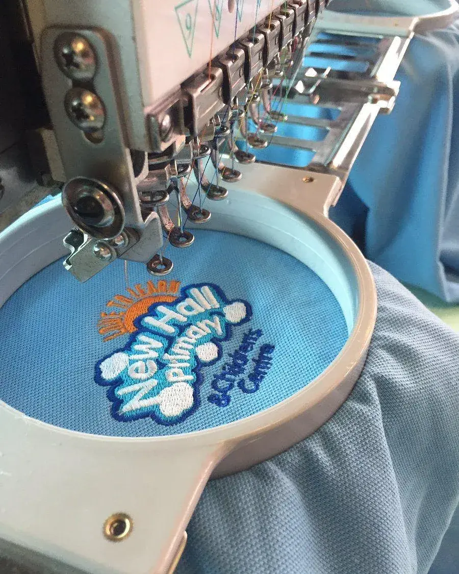 Nadelleiste der Stickmaschine über einem Stickrahmen mit mehrfarbiger Logostickerei in der Werkstatt in Peine